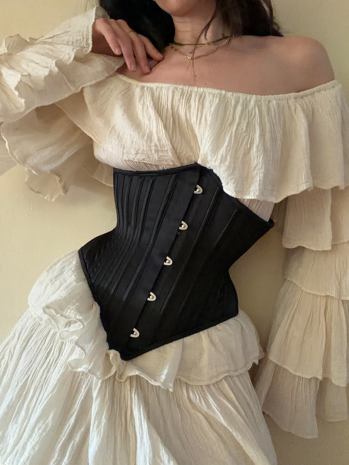 Person wearing a white off-shoulder top with a black corset over a beige background