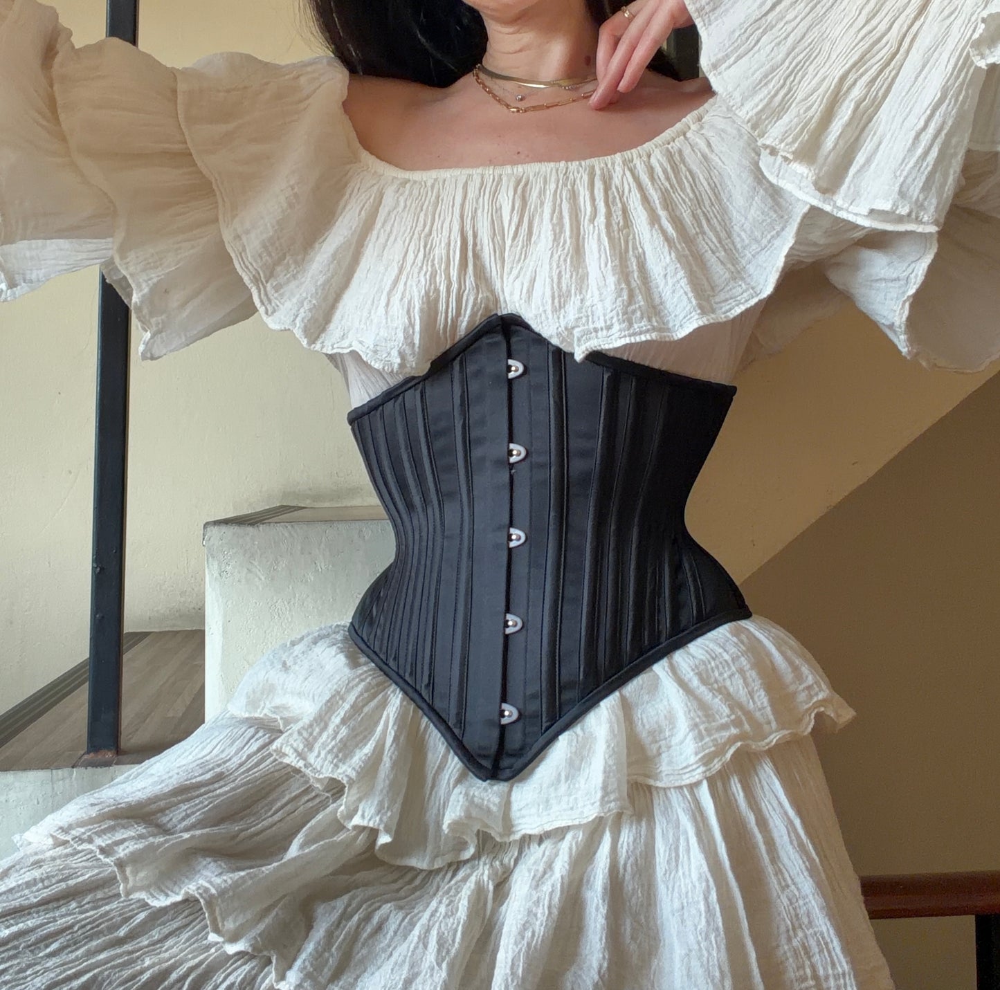 Person wearing a black corset over a white ruffled dress.