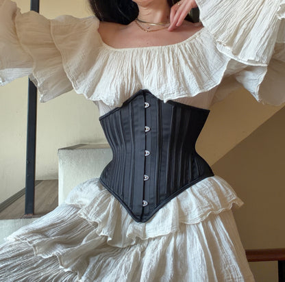 Person wearing a black corset over a white ruffled dress.