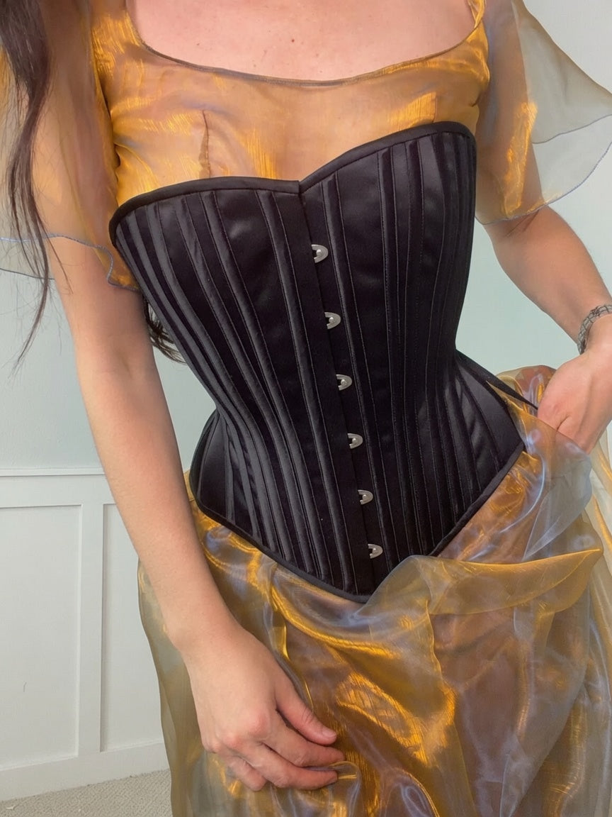 Person wearing a black corset over a yellow top and skirt.