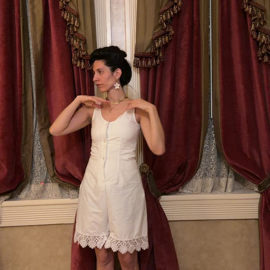 video of a woman in a white sleeveless romper in front of curtains