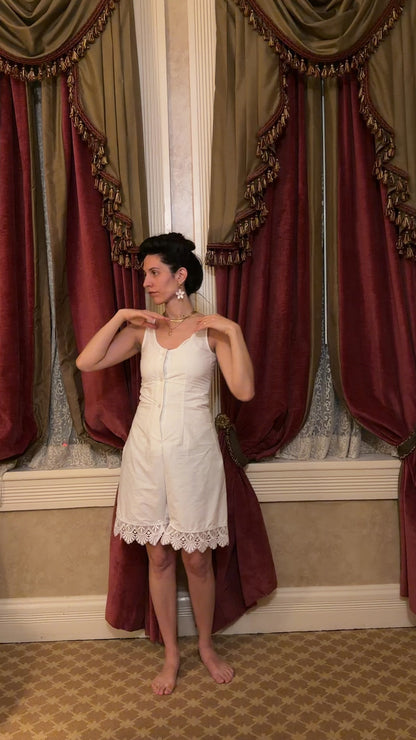 video of a woman in a white sleeveless romper in front of curtains