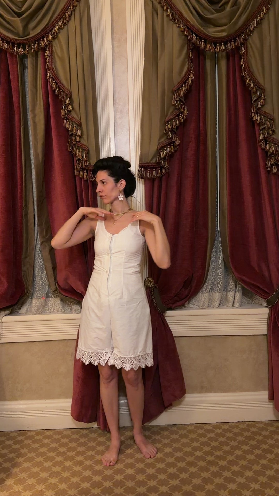 video of a woman in a white sleeveless romper in front of curtains